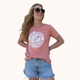 woman wearing the lifes a wave ride it brave tshirt. the color is sunset orange and its a relaxed fit.