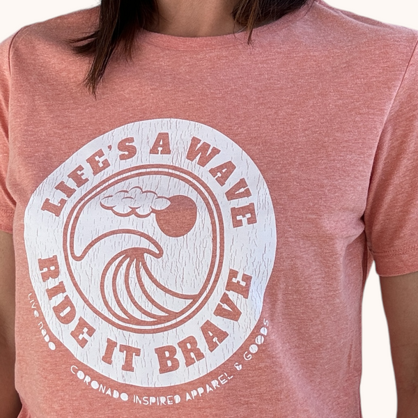 close up of the sunset orange color women's tshirt with a lifes a wave ride it brave saying