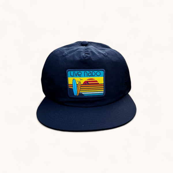 flat brim unstructured surf cap, navy blue with retro colored embroidered surf board patch that looks like a Coronado sunset